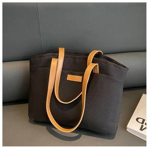 Detail of black canvas tote bag showing brown leather handles and brand logo patch