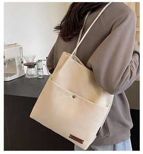Detail of canvas tote bag showing front pocket with metal snap and brown leather tag