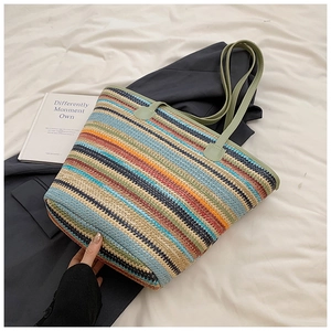 Close-up of colorful striped woven straw tote bag with green leather handles on a bed