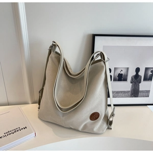 Detail of cream canvas tote bag showing the round leather logo and metal strap buckle