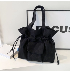 Detail of black corduroy tote bag featuring drawstring closure and front flap pocket