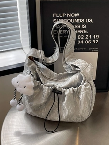 Metallic silver pleated hobo bag with cloud charm and wide strap on silver table