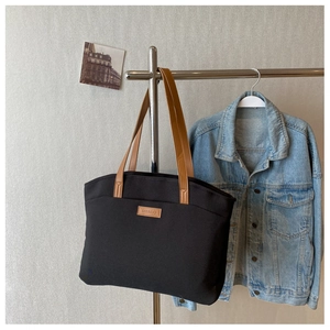 Close-up of contrast leather logo on black canvas tote bag hanging on a hanger