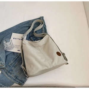 Detail of beige canvas tote bag with adjustable shoulder strap and brown leather patch