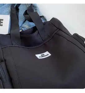Detail of black canvas tote bag with woven label showing the zipper side pocket and texture