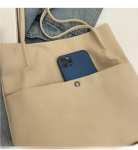 Detail view of the beige canvas tote bag front pocket with metal snap button closure