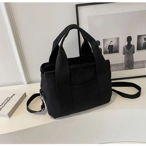 Detail view of the black canvas tote bag showing the adjustable shoulder strap and metal buckle