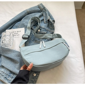 Top view of a light blue canvas crescent bag with double zipper on a cozy bed setup