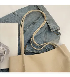 Detailed view of beige canvas tote bag with reinforced handles on denim and magazine