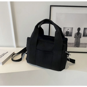 Close-up of black canvas tote bag with front pocket and adjustable shoulder strap