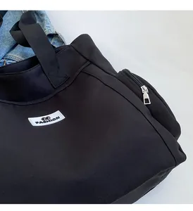 Detail of spacious black canvas tote bag showing side zipper pocket and fashion patch