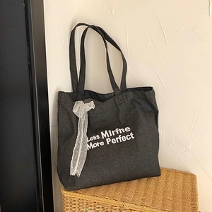 Dark grey denim tote bag with white embroidery and lace ribbon on a woven basket