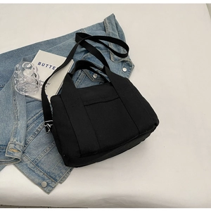 Black canvas tote bag layered over a blue denim jacket in a stylish urban outfit setting