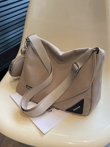 Sac messager minimaliste en toile beige avec petite pochette assortie posé sur une chaise