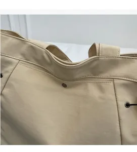 Detailed close-up of beige fabric texture and dark grey metal rivets on a handbag