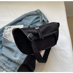 Macro detail of a black nylon crossbody bag with zipper compartments on a white sheet
