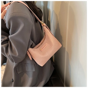 Détail de la texture tressée du sac rose avec plaque logo dorée et fermeture éclair
