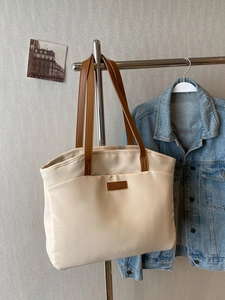 Minimalist beige tote bag with brown handles and leather patch hanging on a wall