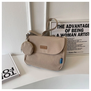 Close-up of beige canvas messenger bag with leather logo tag and mini round coin purse