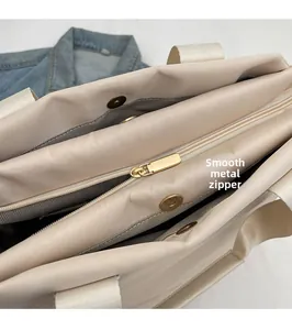 Detail of smooth gold zipper and magnetic closure on beige tote with herringbone lining