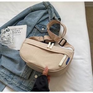 Close-up of beige canvas crossbody bag with dual zippers and woven pulls on fabric
