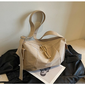 Dettaglio della borsa a tracolla in tela beige con doppie cerniere a treccia e tracolla