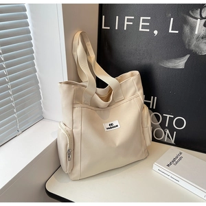 Detail view of off-white canvas tote bag with side zippers and FASHION label