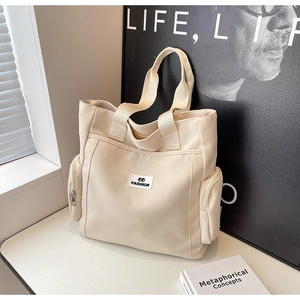 Close-up of off-white canvas tote bag with FASHION label and side zipper pockets