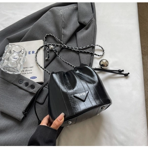Detail shot of black shiny bucket bag with silver chain strap and metal feet