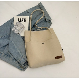 Detail of beige canvas tote bag showing front pocket with metal snap and leather logo label