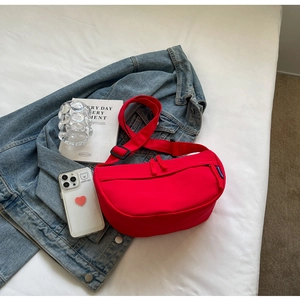 Detail of red crescent nylon crossbody bag with wide strap on casual denim background