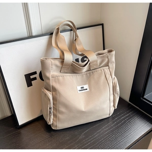 Detail of beige canvas tote bag showing front pockets and embroidered fashion label