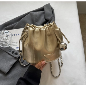 Detail of champagne gold bucket bag featuring a drawstring closure and silver ball charm