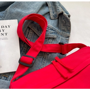 Detail of red crossbody bag with wide shoulder strap and black buckle on denim fabric