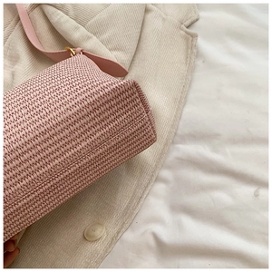 Gros plan d'un sac bandoulière en paille rose clair avec boucle en métal doré