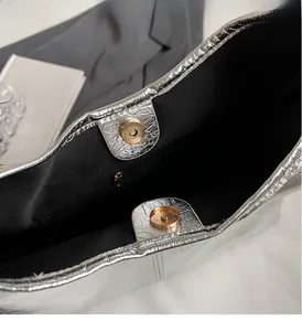Detail of silver metallic crinkled handbag showing golden magnetic closure and black lining