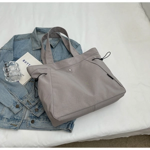 Detail view of a gray nylon tote bag featuring adjustable side drawstrings and metal clasp