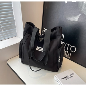 Detail view of spacious black canvas tote bag with front logo and side zipper pockets