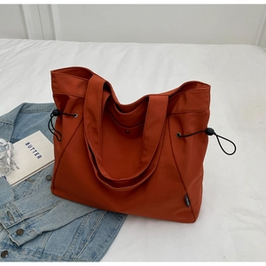Detailed view of caramel nylon tote bag with drawstring side cords on white fabric
