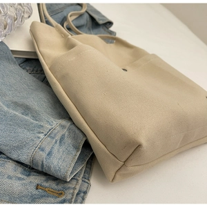 Detailed macro view of beige canvas tote bag showing front pocket and fine fabric texture
