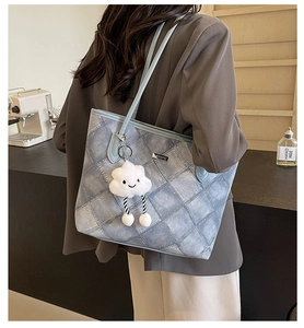 Detailed side view of blue denim texture tote bag with quilted pattern and plush charm