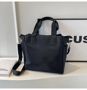 Detail of black tote bag showing side pocket, gold hardware, and detachable shoulder strap