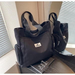 Close-up of black canvas tote bag with front pocket and FASHION label detail