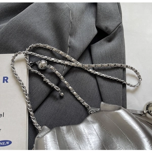 Detail of silver metallic pleated bucket bag with chain strap on a grey blazer