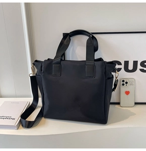 Detail of black nylon tote bag featuring reinforced handles and adjustable wide strap