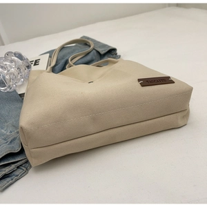 Close-up of cream canvas tote bag showing the leather logo tag and durable textured fabric