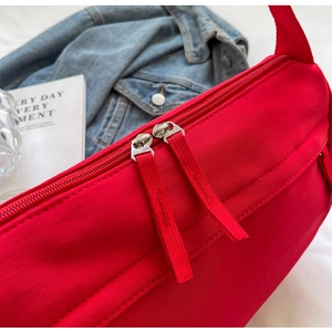 Close-up of dual metal zippers and red fabric pulls on a casual nylon crossbody bag