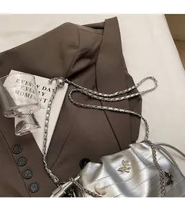 Détail d'un sac seau plissé argenté métallisé avec un accessoire papillon en métal chic