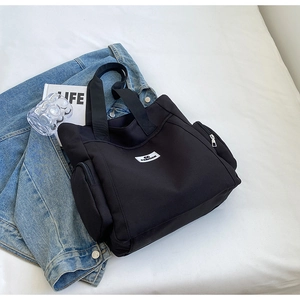 Close-up of black canvas tote bag featuring double zippered side pockets and logo
