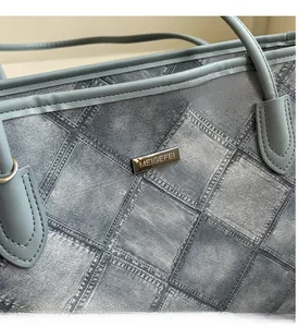 Close-up of blue plaid fabric tote with light gold metal logo and leather trim